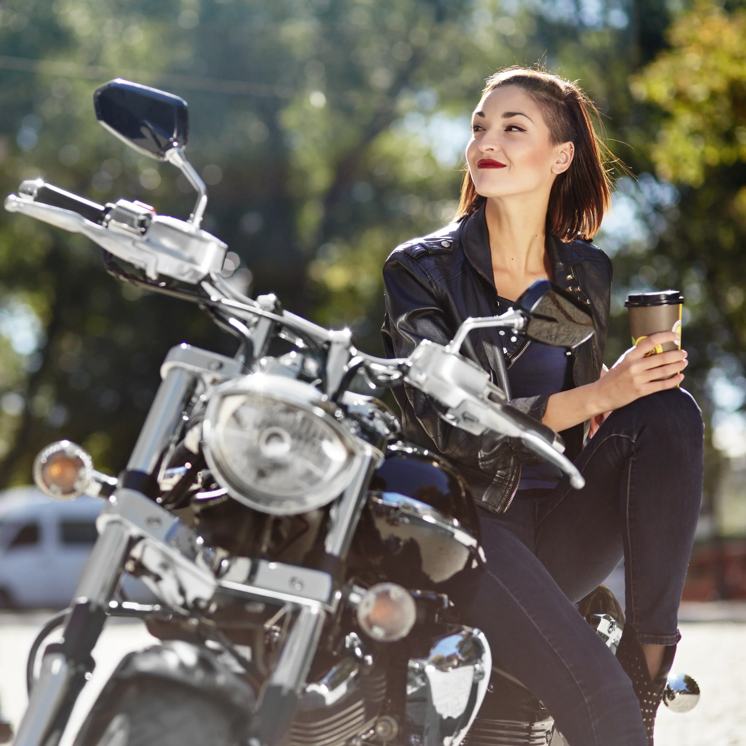 mulher sentada em moto segurando café e olhando para o lado